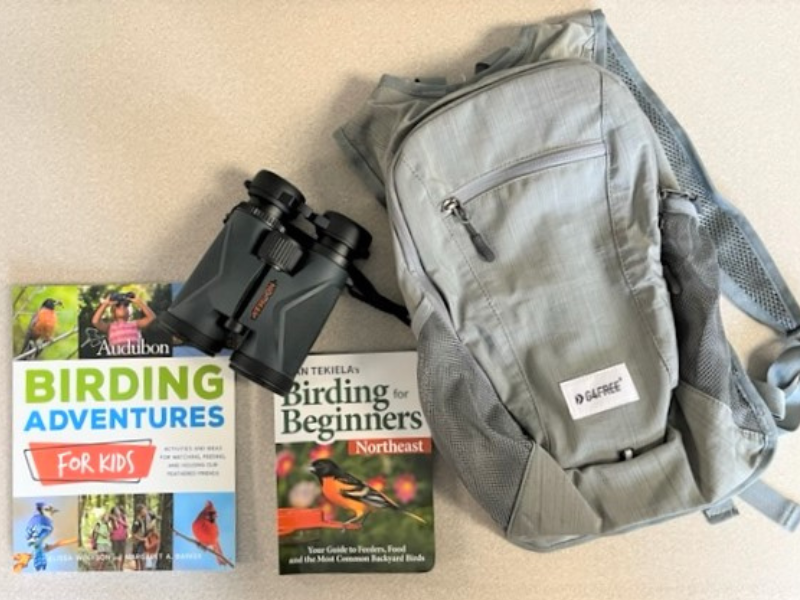 Binoculars birding books and a gray backpack on a table
