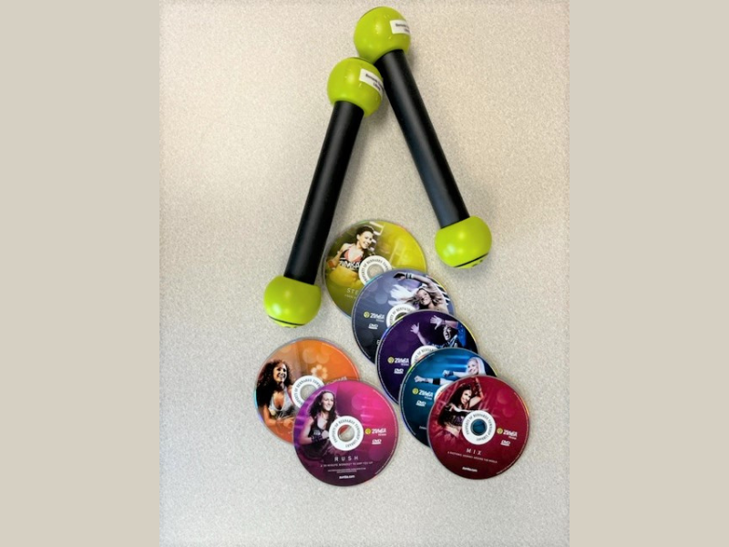 Two green dumbbells beside a collection of Zumba workout DVDs