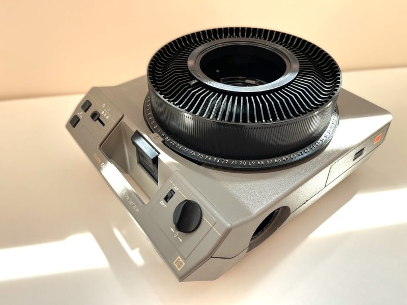 A vintage slide projector with a circular film holder and controls